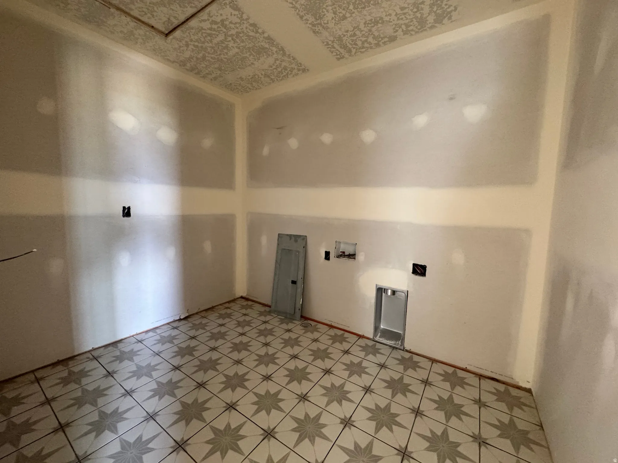 Room featuring patterned tile flooring, exposed drywall, and an electrical panel