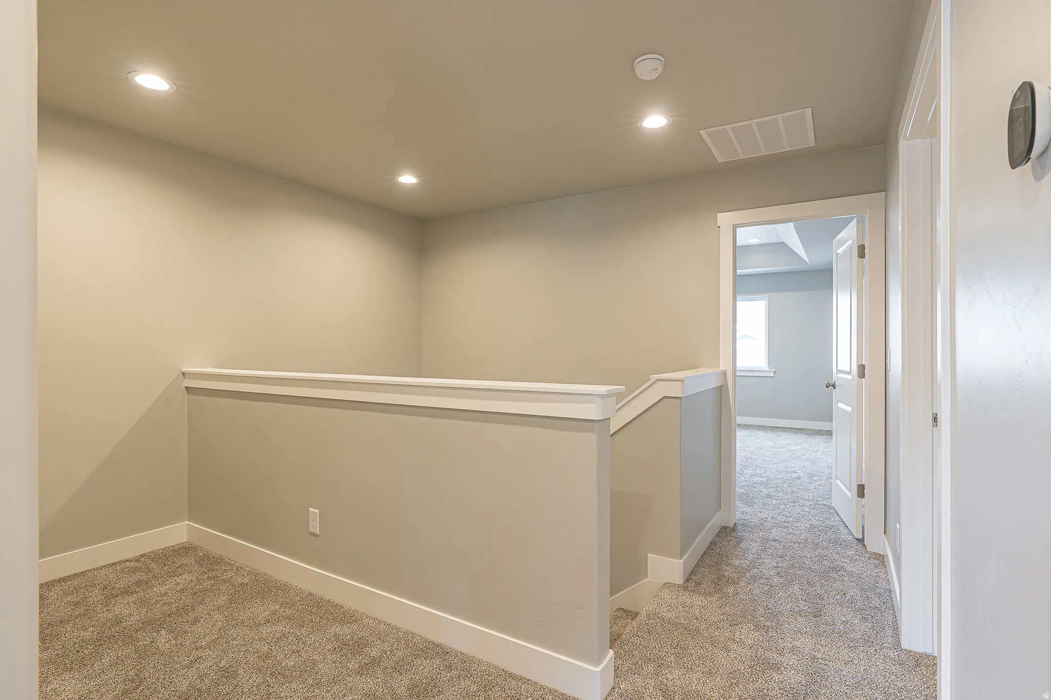 Carpeted upper level landing with a painted half-wall railing, recessed ceiling lights, and light gray wall paint