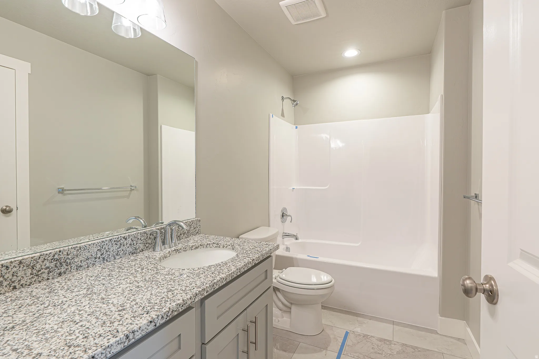 Bathroom featuring a speckled vanity countertop, undermount sink, built-in bathtub with shower, light gray cabinetry, and tile flooring