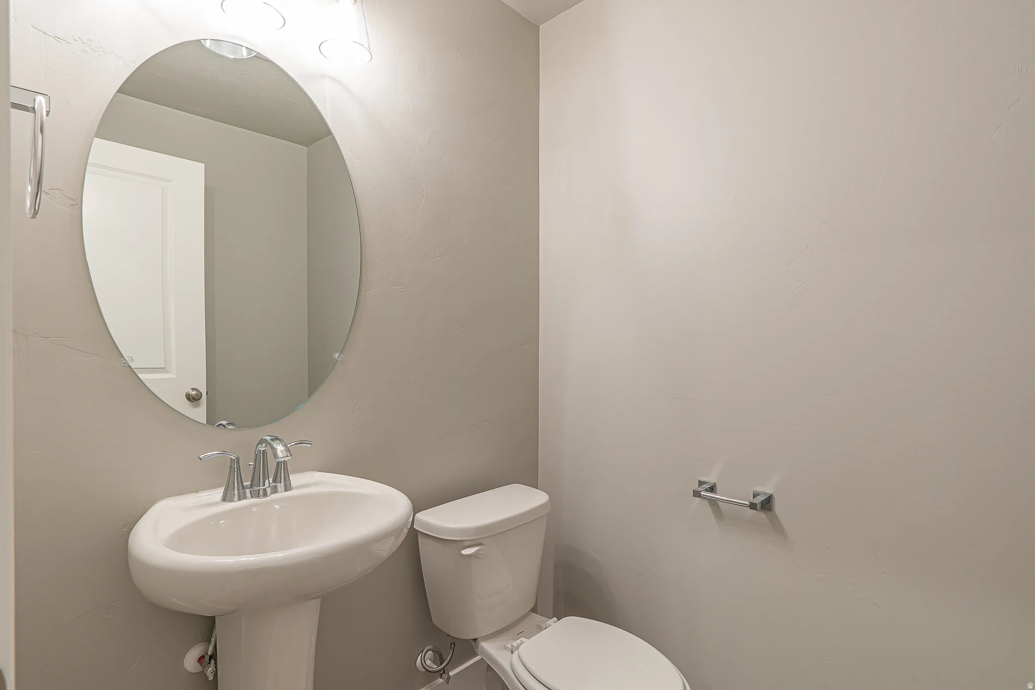 Pedestal sink with chrome faucet, oval mirror, and overhead vanity lighting