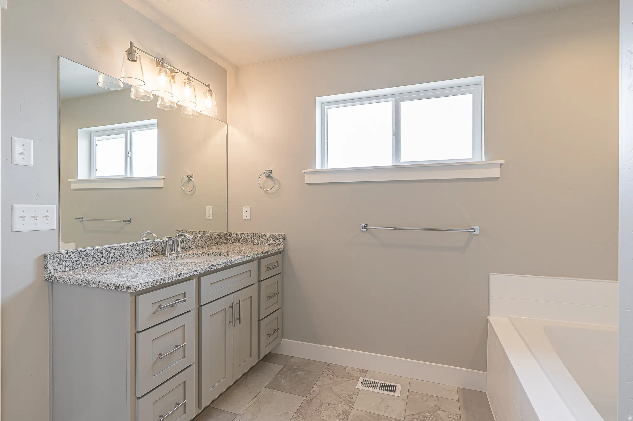Bathroom featuring a double vanity with light-colored cabinetry, a speckled countertop, and dual undermount sinks