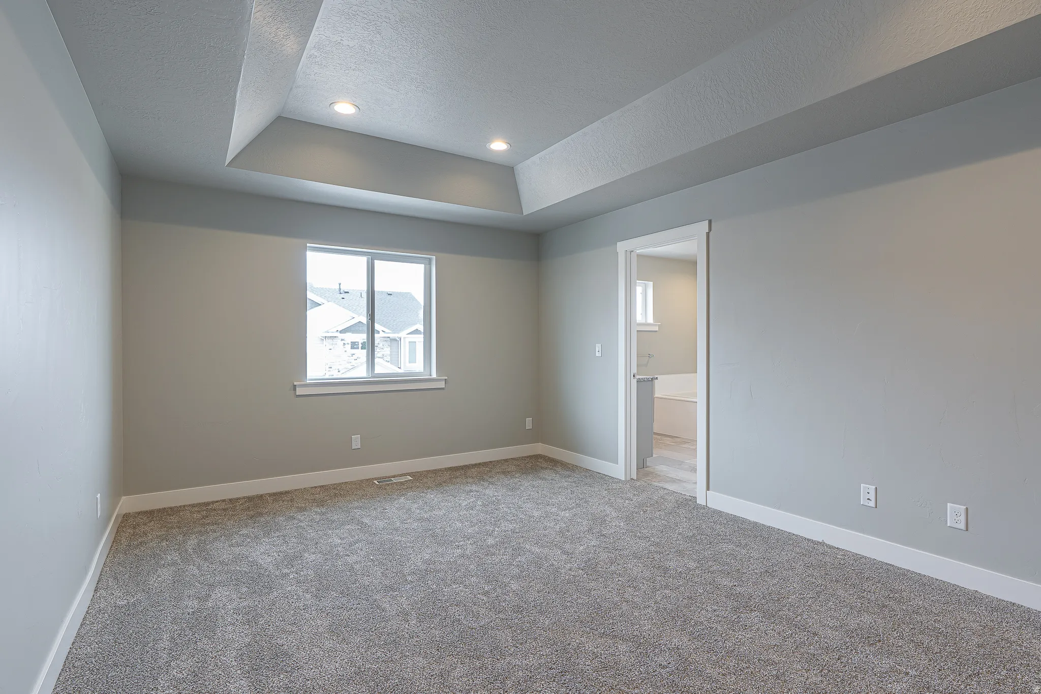 Room featuring a tray ceiling with recessed lighting, a window with white trim, gray walls, and gray carpeting