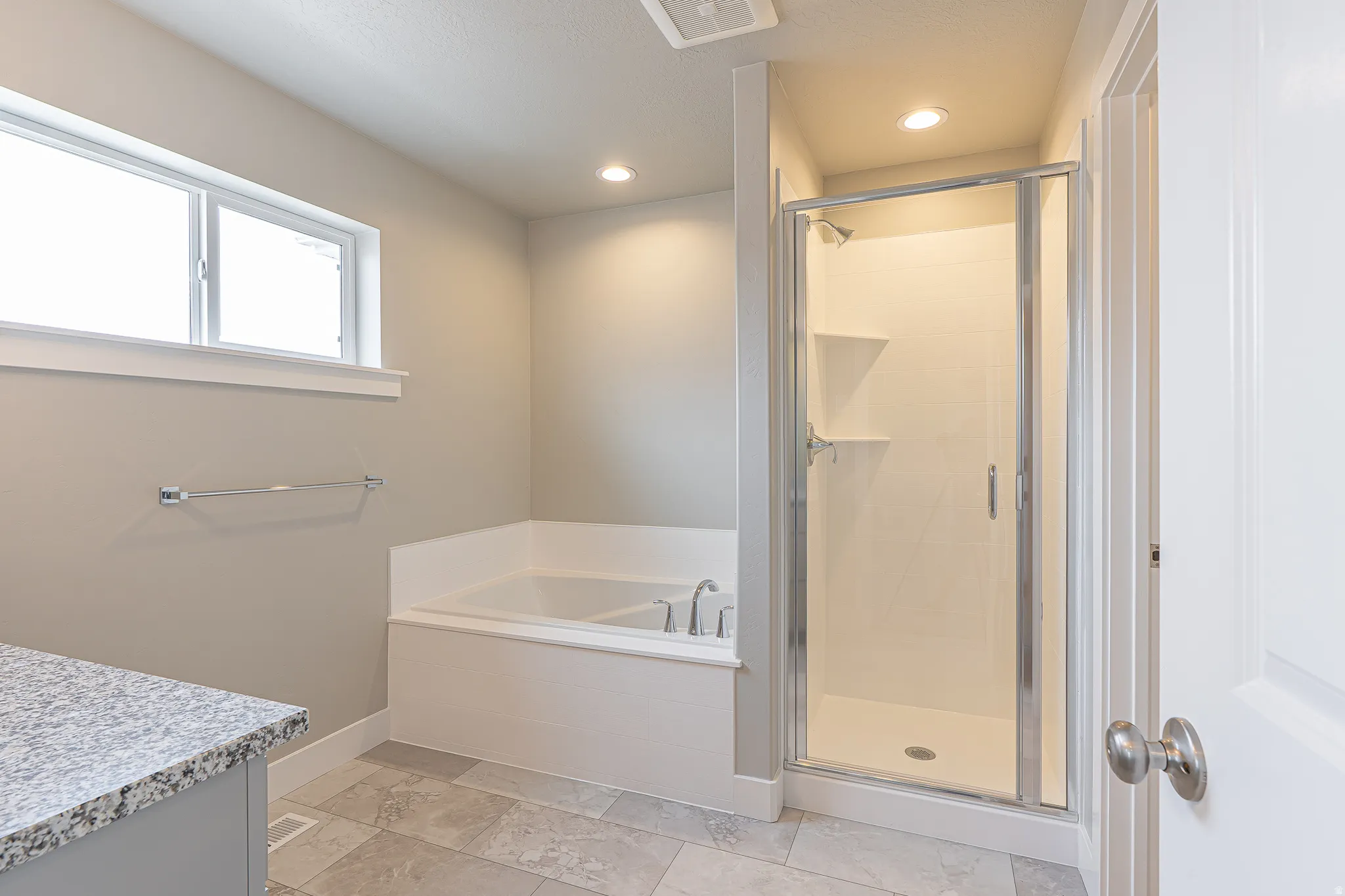 Bathroom featuring a built-in soaking tub, a glass-enclosed shower with integrated shelving, and a vanity with a granite-style countertop