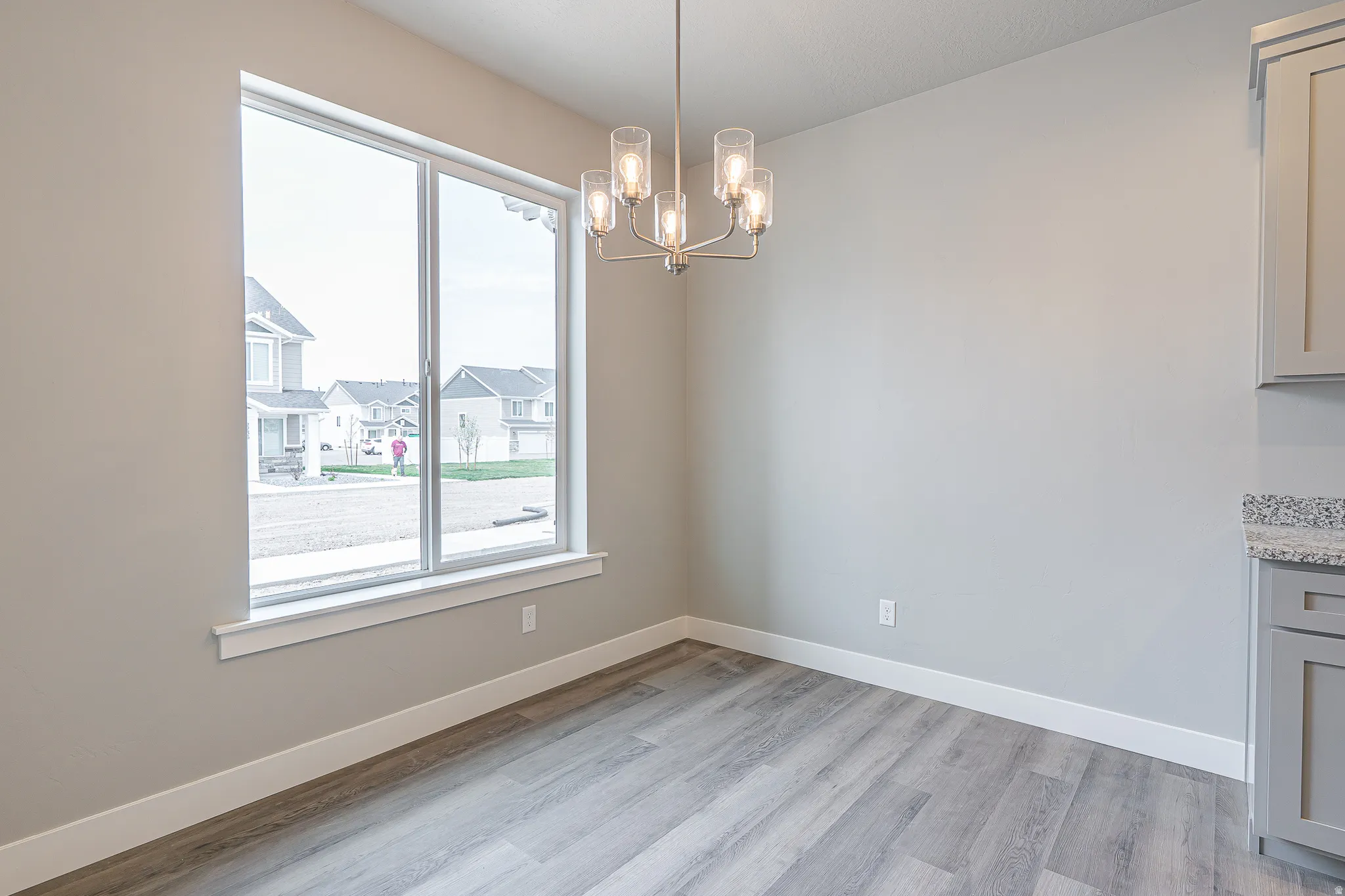 Dining area featuring a large window, wood-finish flooring, a contemporary chandelier, light gray walls, and white baseboards