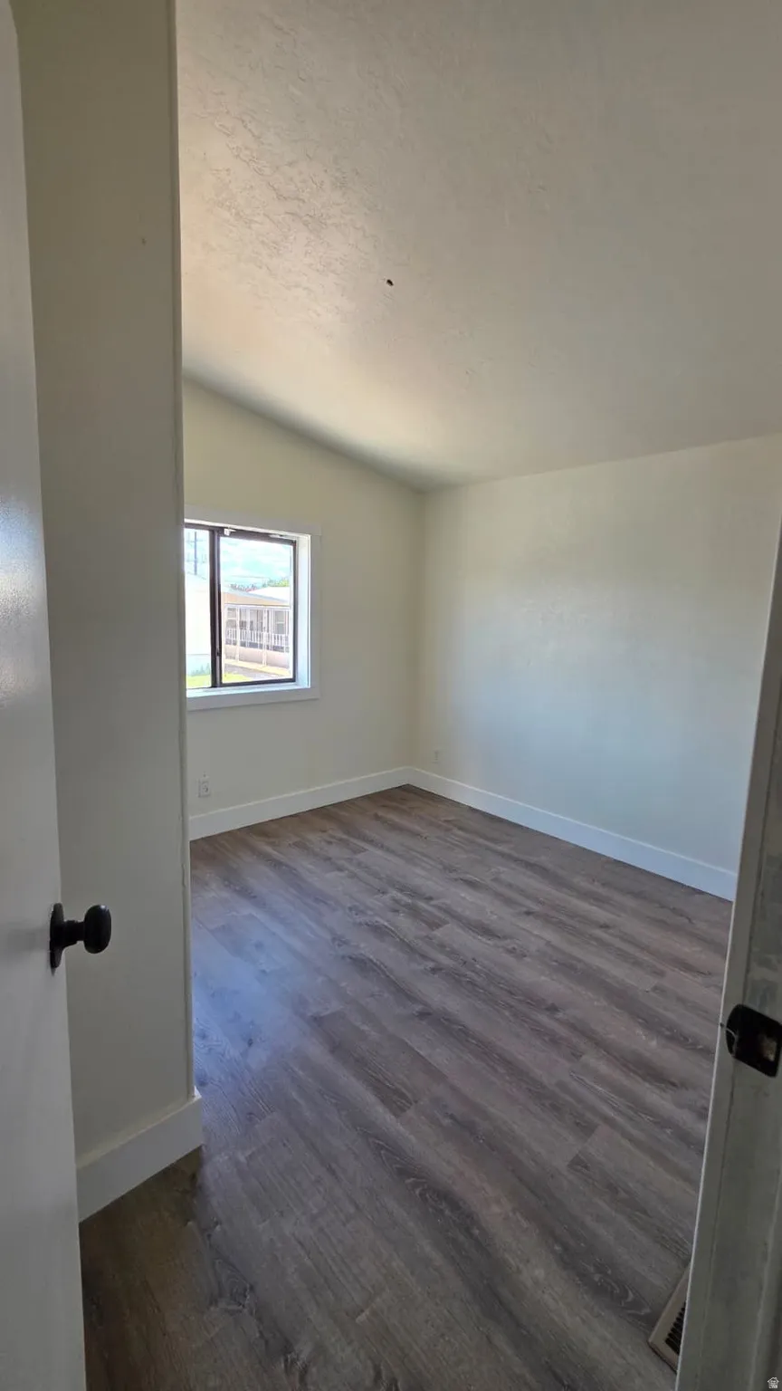 Spacious room featuring vaulted ceilings, wood-finish flooring, white baseboards, and a window with a white frame