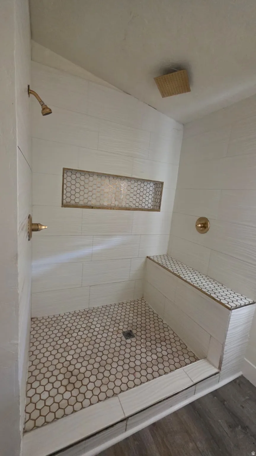 Shower featuring white subway tile walls, a built-in bench with mosaic tile, a recessed niche with mosaic tile, hexagon mosaic floor tile, and gold-finish fixtures