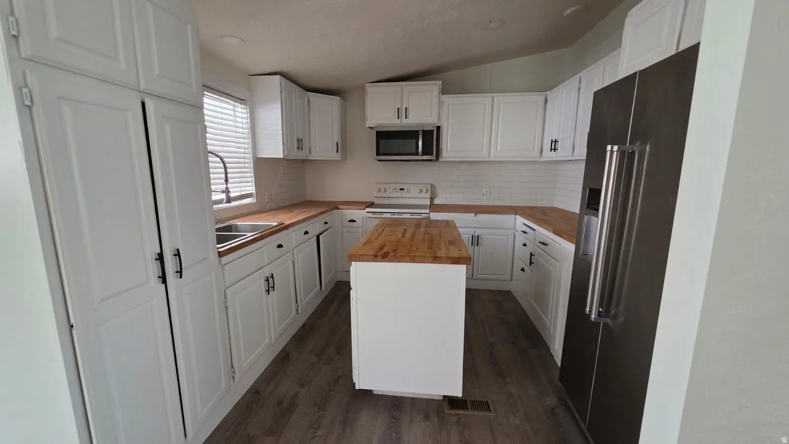 Kitchen featuring white cabinetry, wood-finish countertops, stainless steel appliances, a center island, and wood-finish flooring