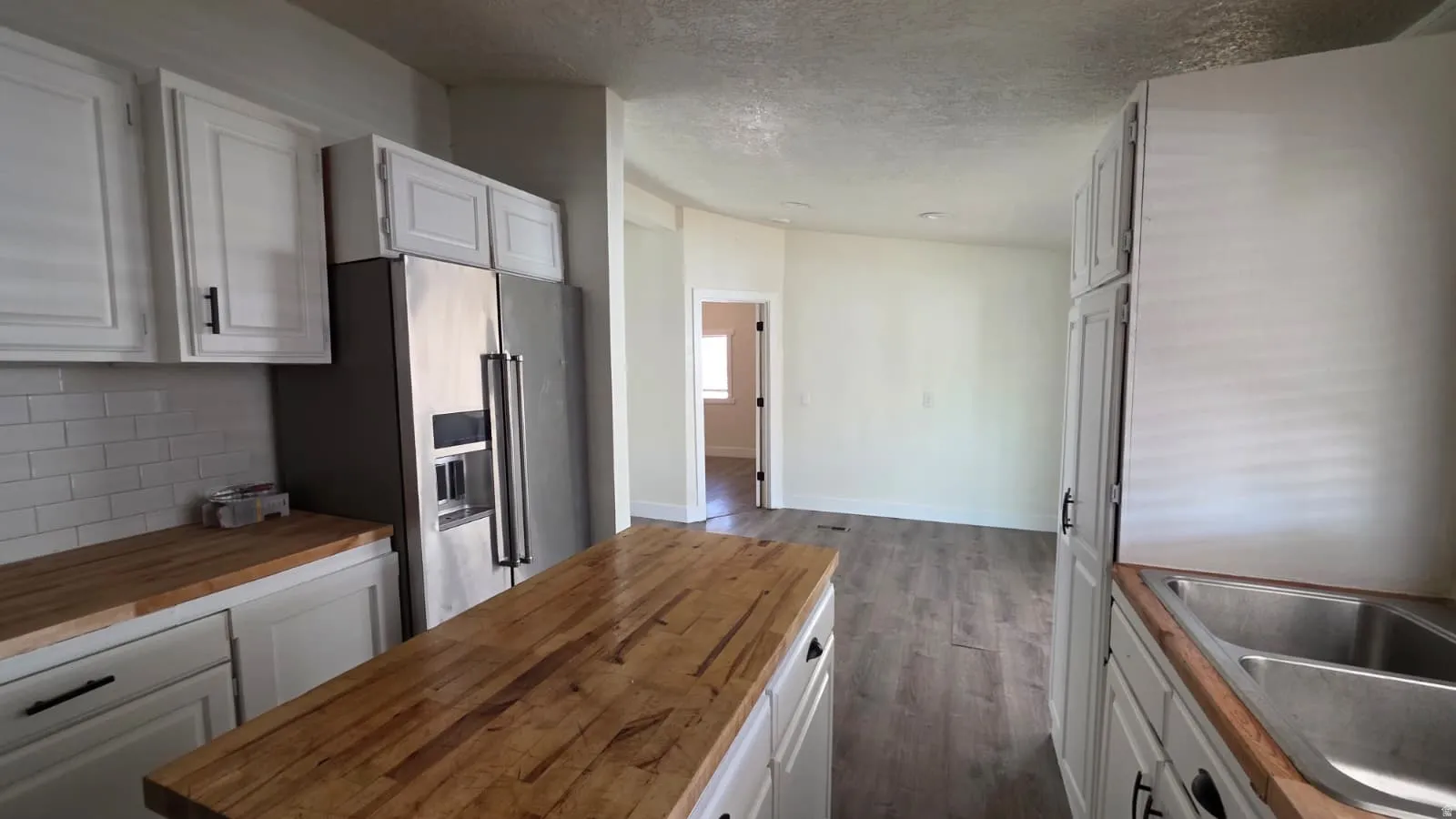 Kitchen featuring wood-finish countertops, white cabinetry with dark hardware, a stainless steel refrigerator, and subway tile backsplash