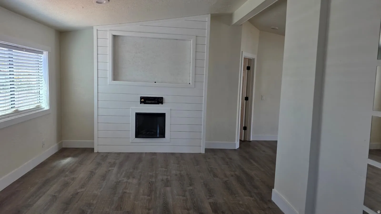 Living area featuring wood-finish flooring, a contemporary electric fireplace with shiplap surround, and a built-in media niche