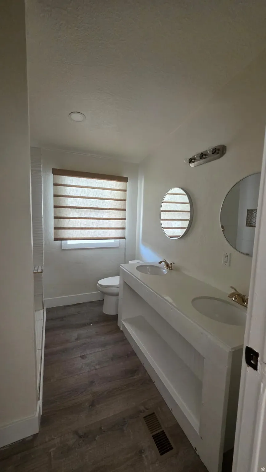 Double vanity featuring white countertops and dual undermount sinks, wood-finish flooring, recessed lighting, and a window with horizontal blinds