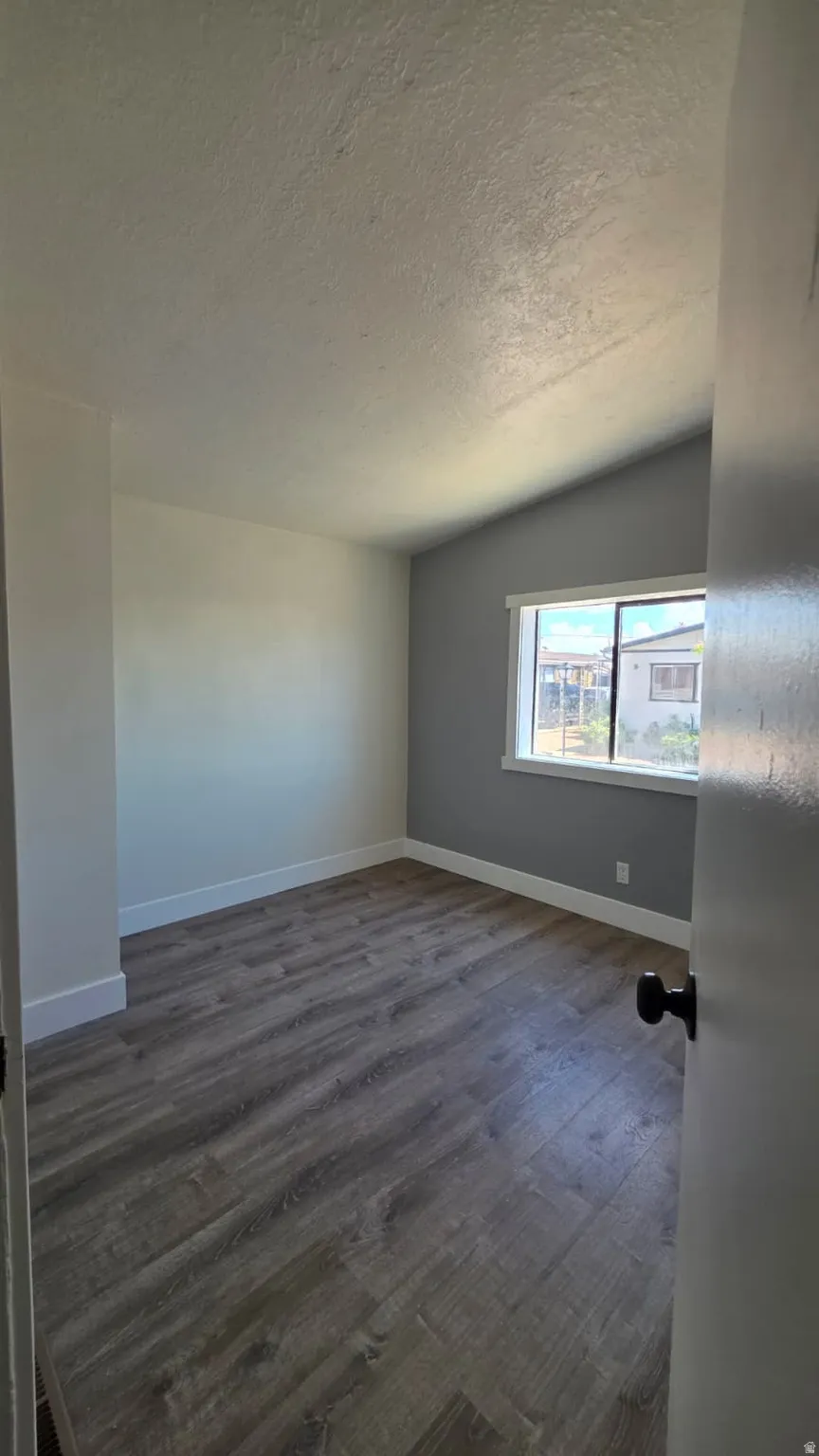 Room featuring wood-finish flooring, white baseboards, and a vaulted ceiling