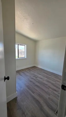 Spacious room featuring vaulted ceilings, wood-finish flooring, white baseboards, and a window with a white frame