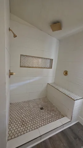 Shower featuring white subway tile walls, a built-in bench with mosaic tile, a recessed niche with mosaic tile, hexagon mosaic floor tile, and gold-finish fixtures