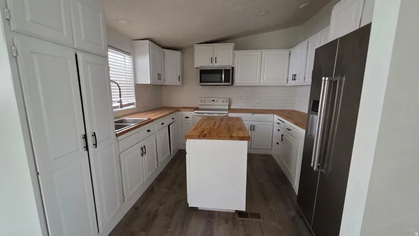 Kitchen featuring white cabinetry, wood-finish countertops, stainless steel appliances, a center island, and wood-finish flooring