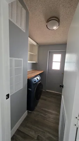 Utility area featuring wood-finish flooring, light gray walls, built-in shelving, a wood-finish countertop, and a rear exterior door with a window