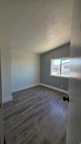 Room featuring wood-finish flooring, white baseboards, and a vaulted ceiling