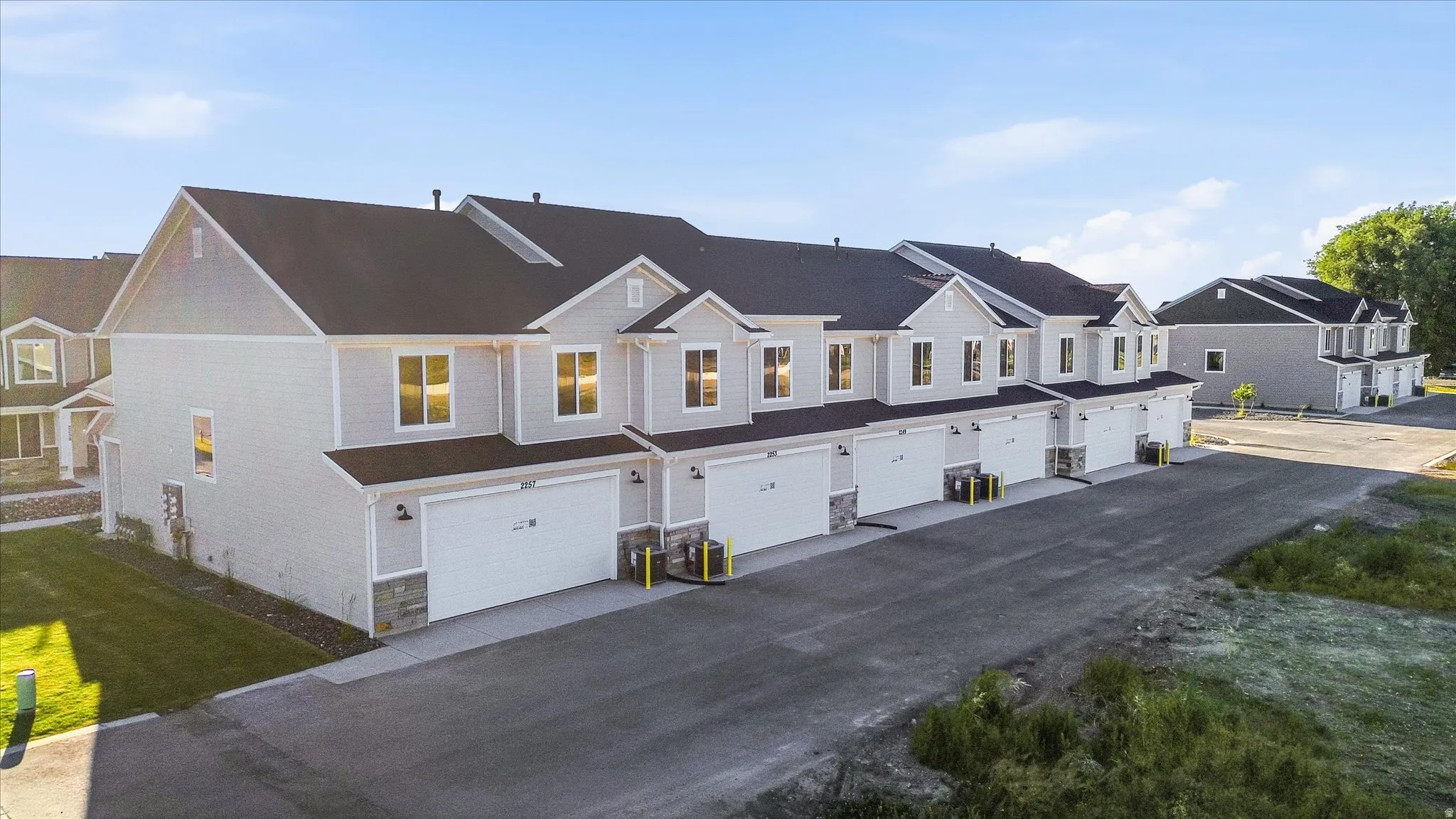 Newly constructed townhome community featuring light gray siding, dark roofing, stone accents, two-car garages, and paved driveways