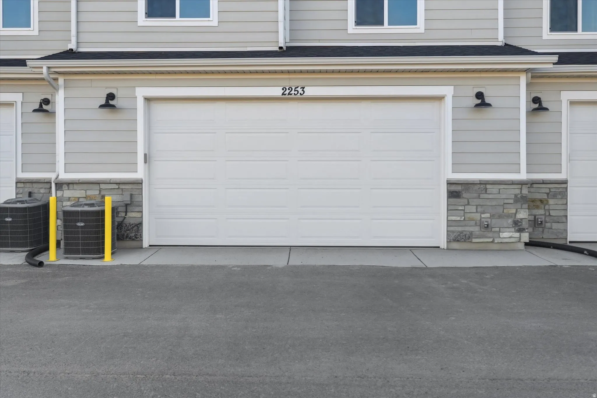 Attached garage featuring a panel-style door, stone veneer detailing, and exterior sconce lighting