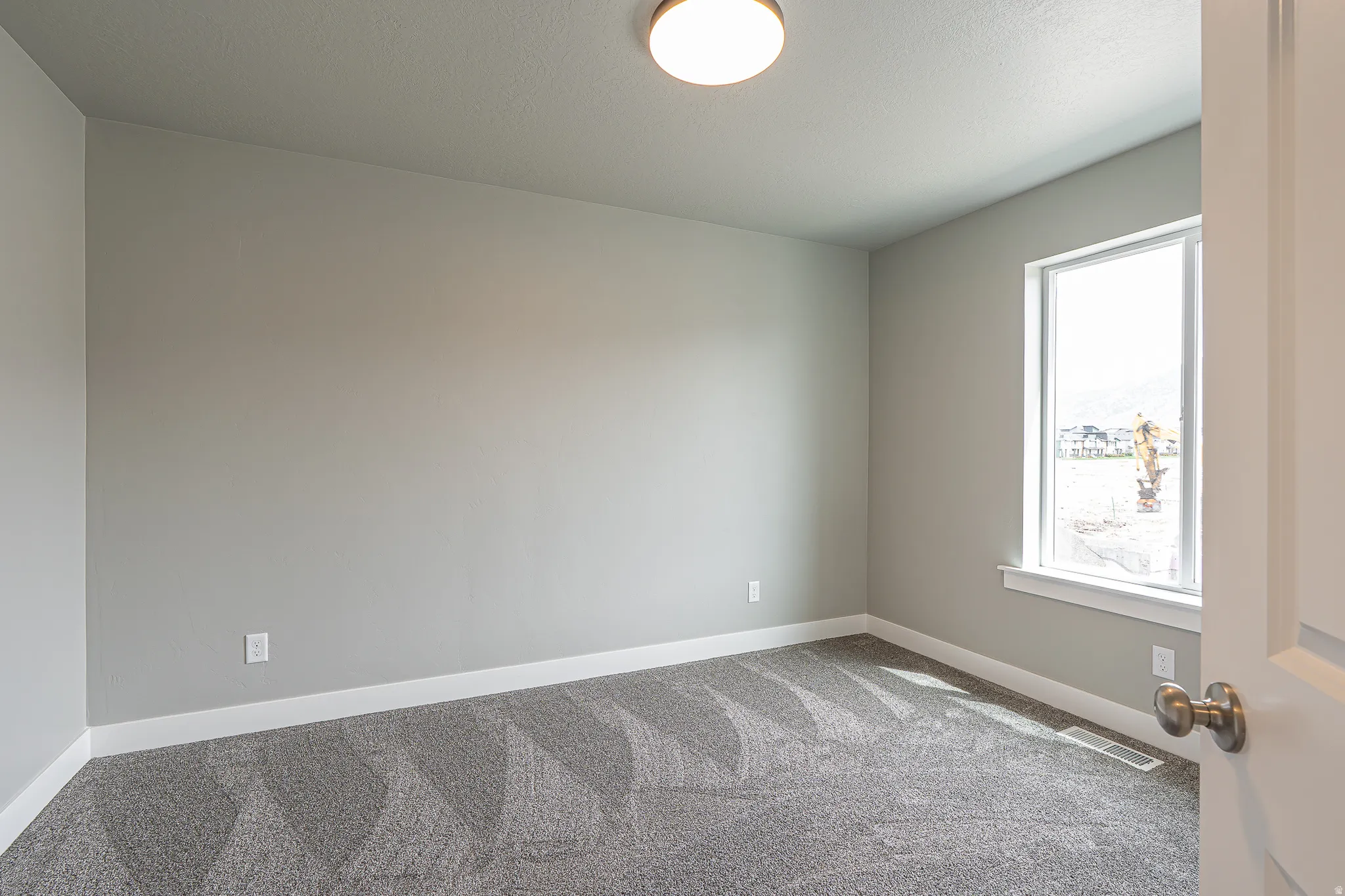Carpeted room featuring light gray walls, a single window with white trim, and a flush-mount ceiling light fixture
