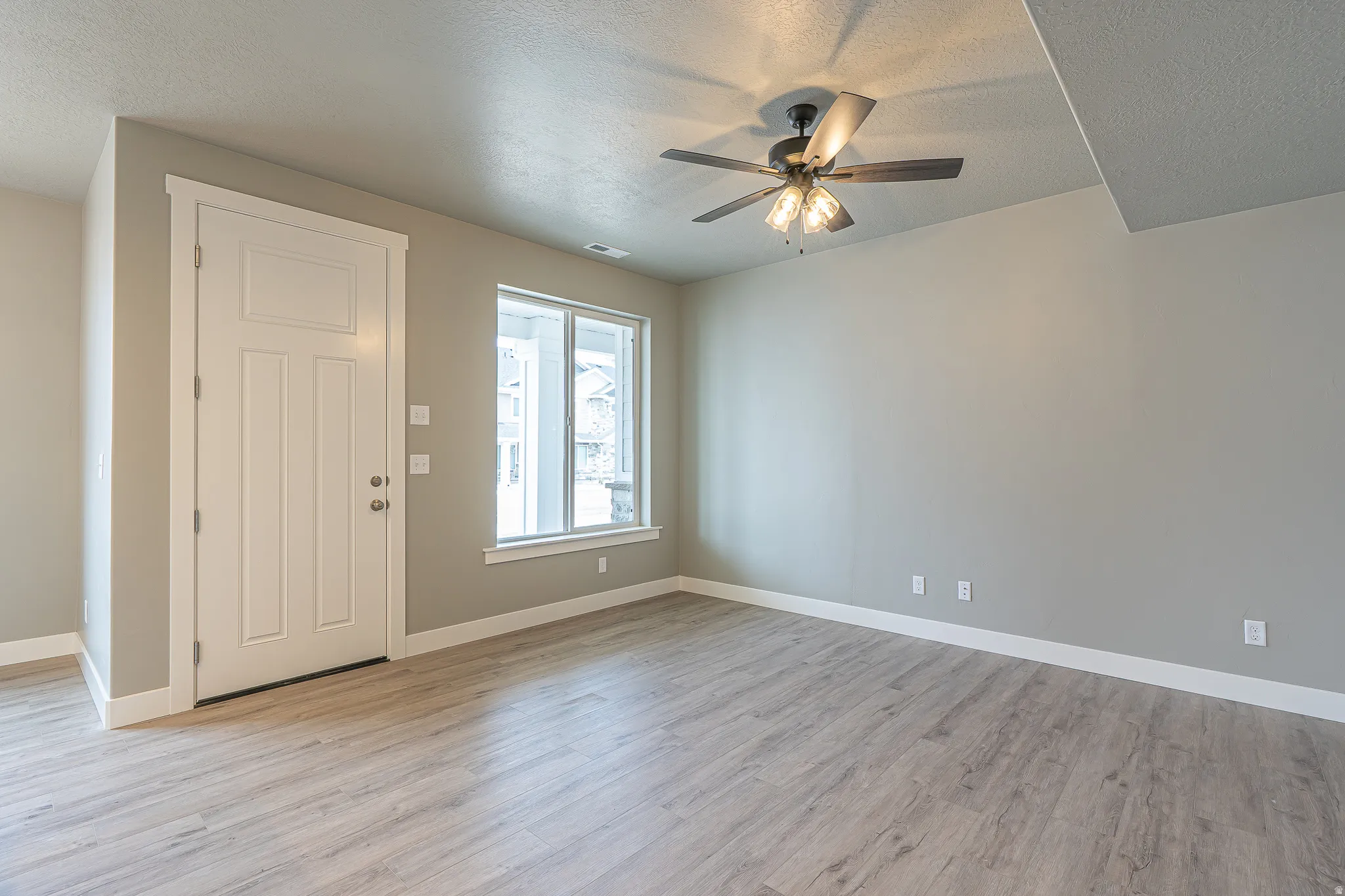 Spacious room featuring wood-finish flooring, a white paneled door, and a multi-pane window with white trim