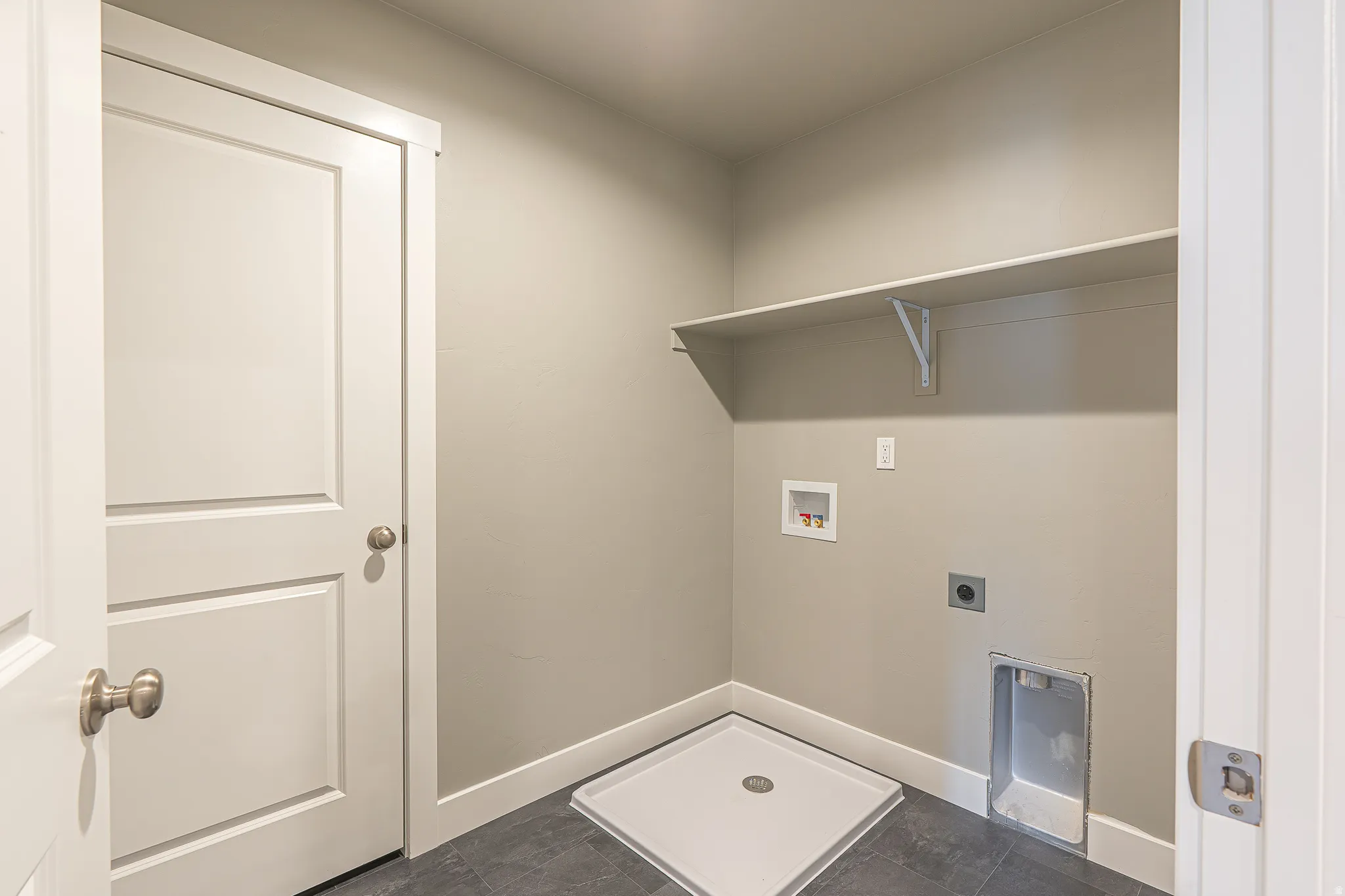 Laundry area with light gray walls, dark gray tile flooring, and white trim
