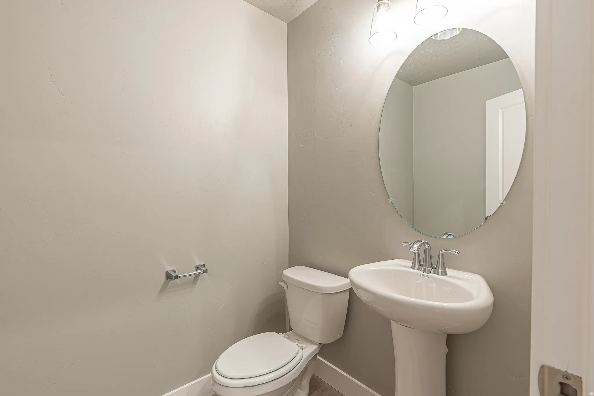 Pedestal sink with chrome faucet, oval mirror, and overhead vanity lighting
