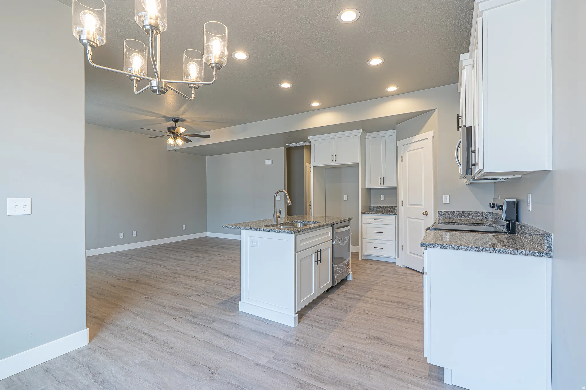 Open-concept kitchen featuring white cabinetry, granite countertops, a central island with an undermount sink, stainless steel dishwasher, and wood-finish flooring