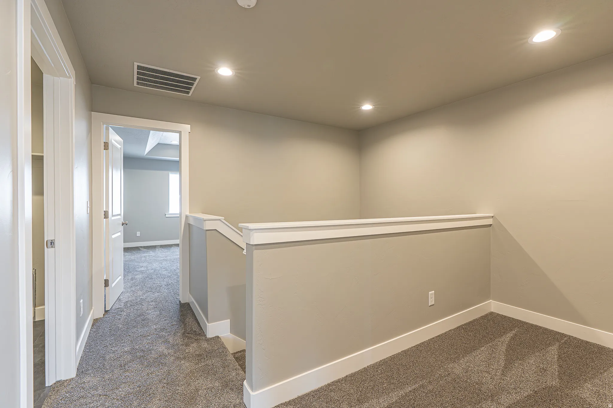 Interior hallway with neutral-toned walls, recessed lighting, and grey patterned carpeting