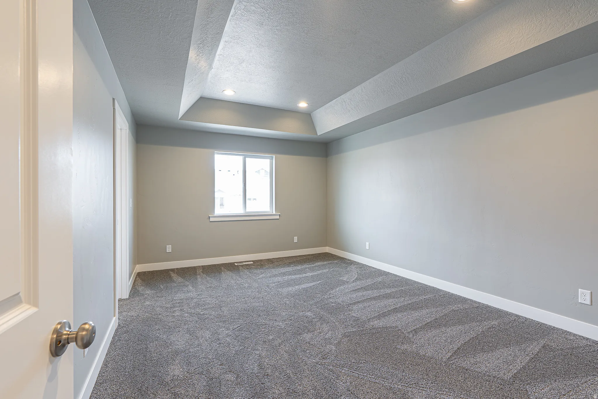 Spacious interior room featuring a tray ceiling with recessed lighting, neutral tone walls, white trim, and gray carpeting