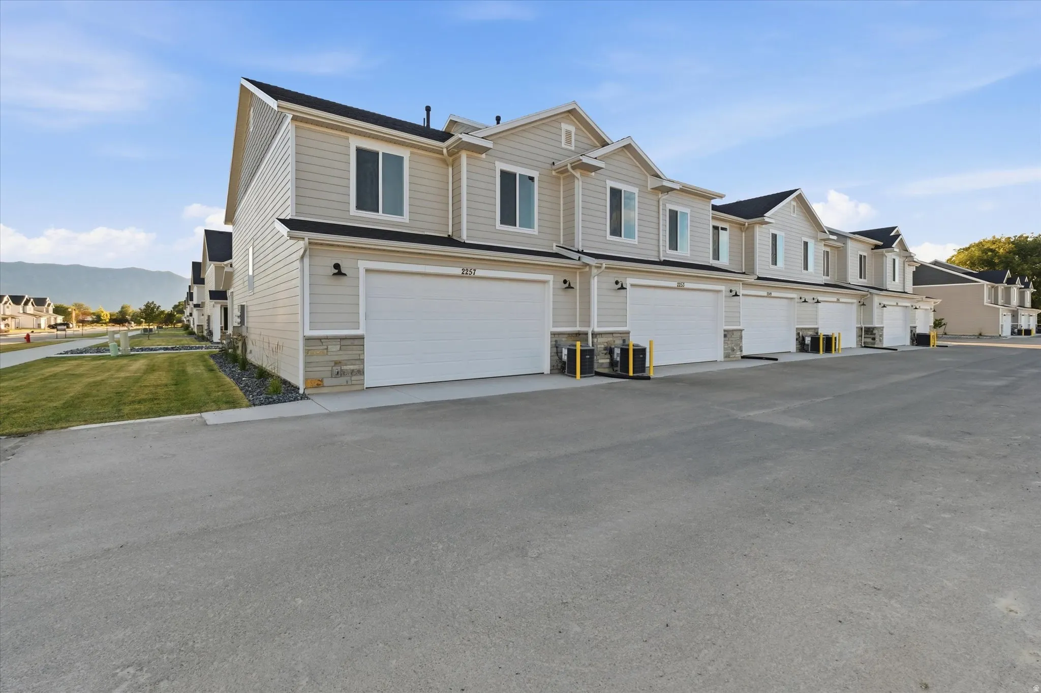Townhome exterior featuring light-colored siding, stone accents, black roofs, and individual garages