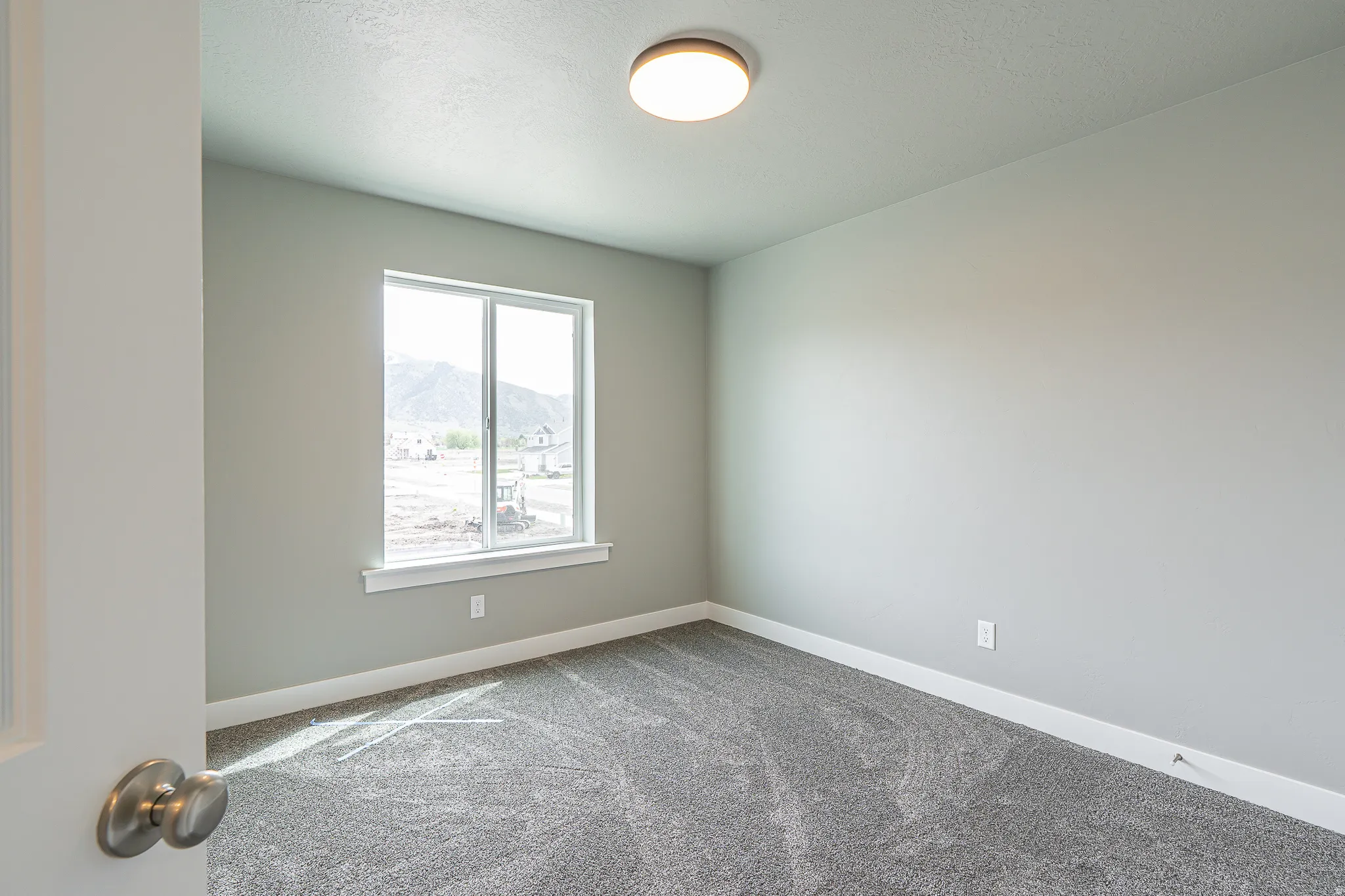 Neutral-toned room featuring a single window, grey carpet flooring, white baseboards, and a flush-mount ceiling light