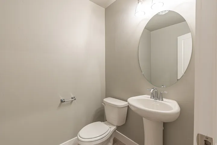 Pedestal sink with chrome faucet, oval mirror, and overhead vanity lighting