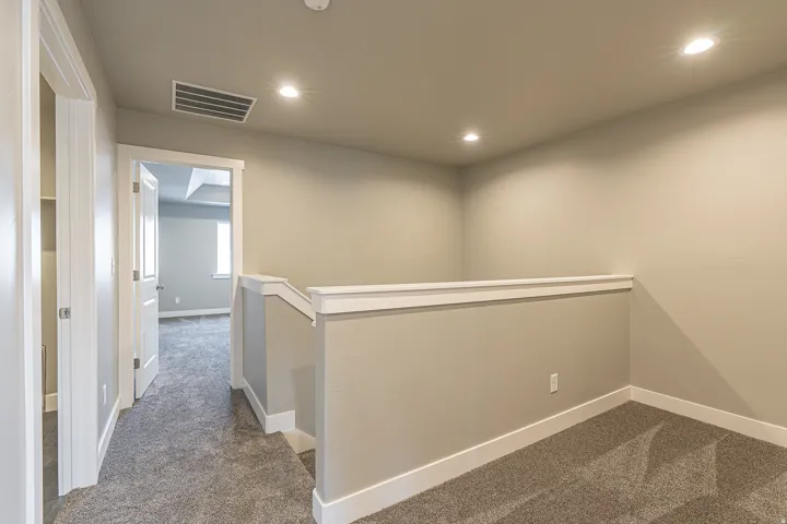 Interior hallway with neutral-toned walls, recessed lighting, and grey patterned carpeting