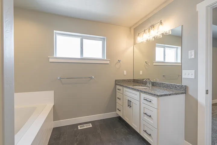 Bathroom featuring a white vanity with a granite countertop, a large mirror, and a modern light fixture