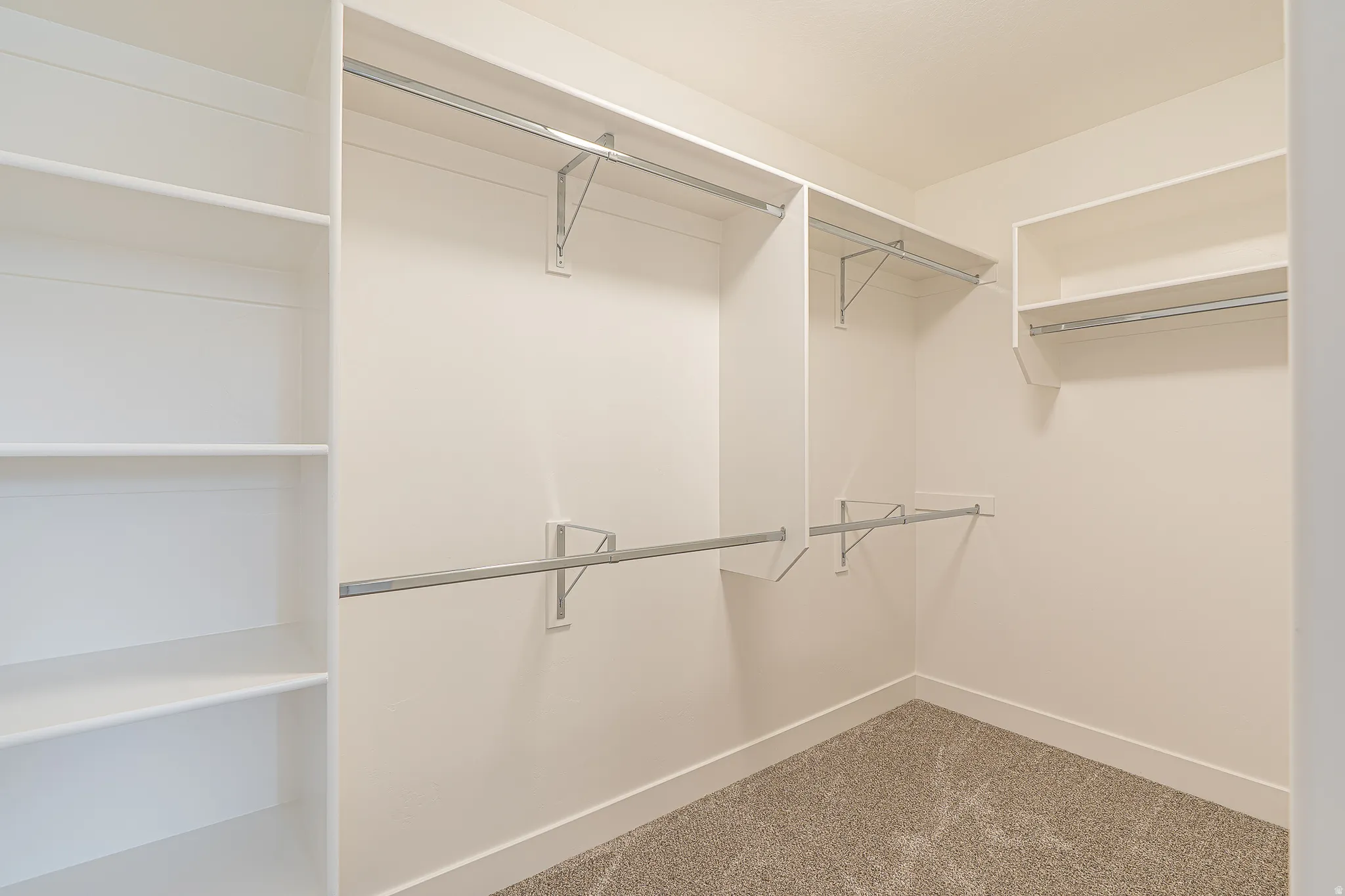 Walk-in closet featuring built-in shelving, multiple hanging rods, white walls, white baseboards, and a neutral-toned carpeted floor