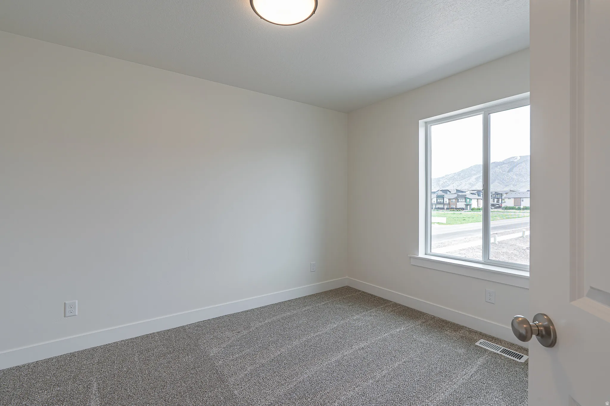 Neutral tone wall paint with white trim, new carpet flooring, and a large window providing natural light