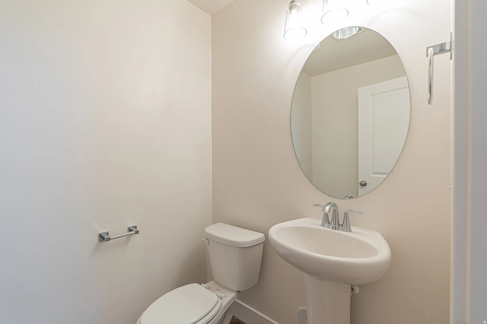 Pedestal sink with chrome faucet, an oval mirror, and a contemporary vanity light fixture
