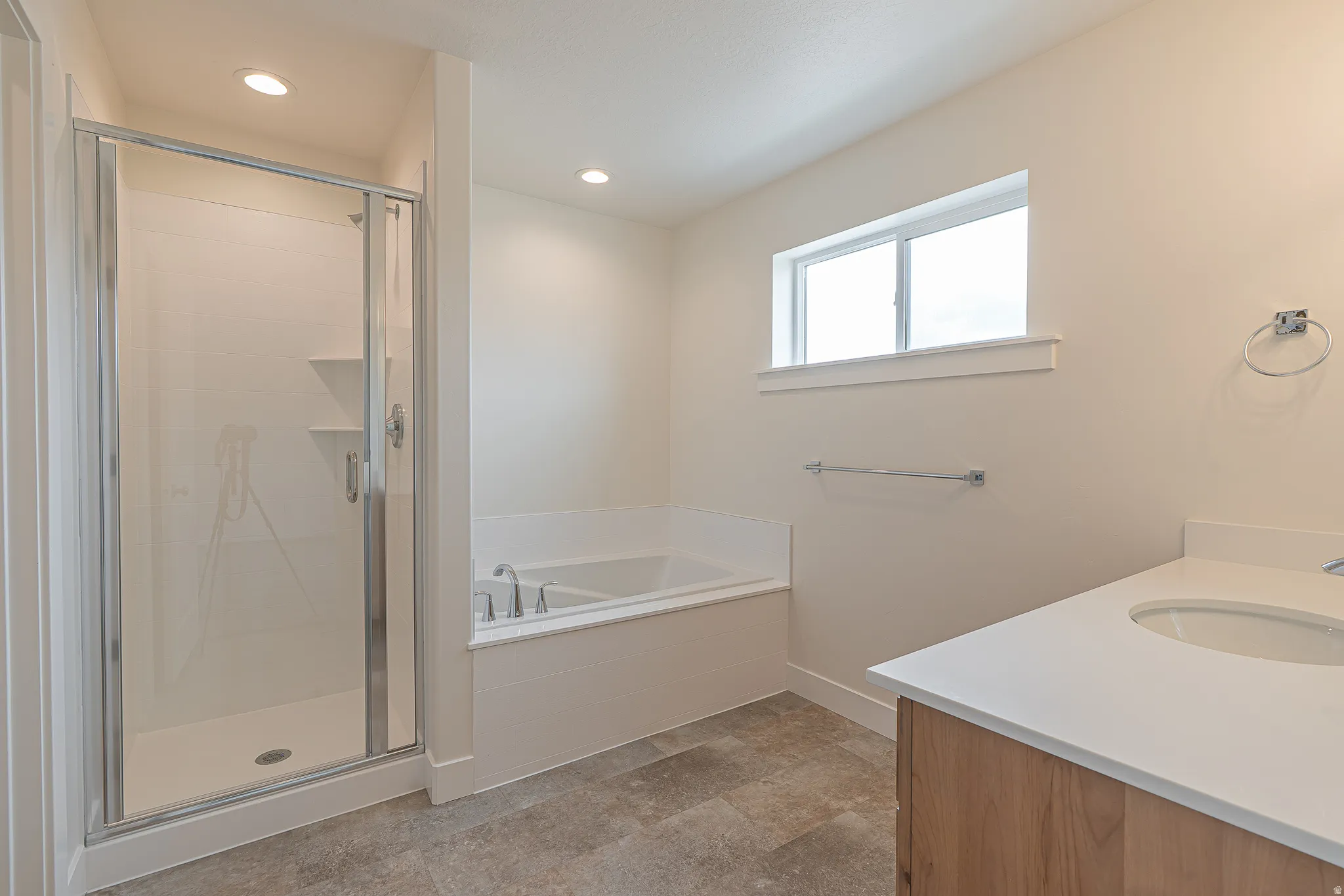 Spacious bathroom featuring a glass-enclosed shower, built-in soaking tub, wood-finish vanity with an undermount sink, and light-toned flooring