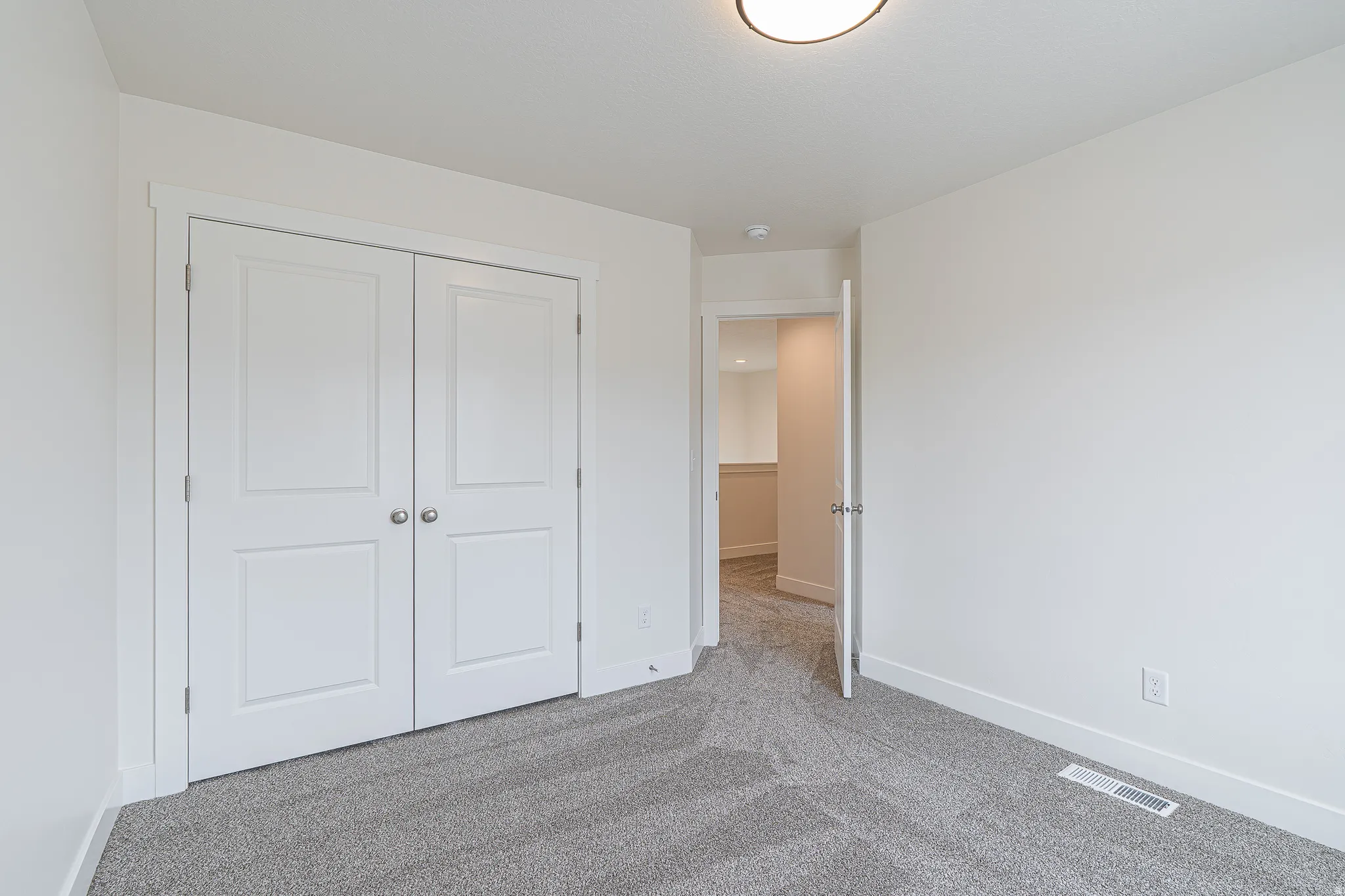 Bright room featuring a flush-mount ceiling light, white walls, and light gray textured carpeting