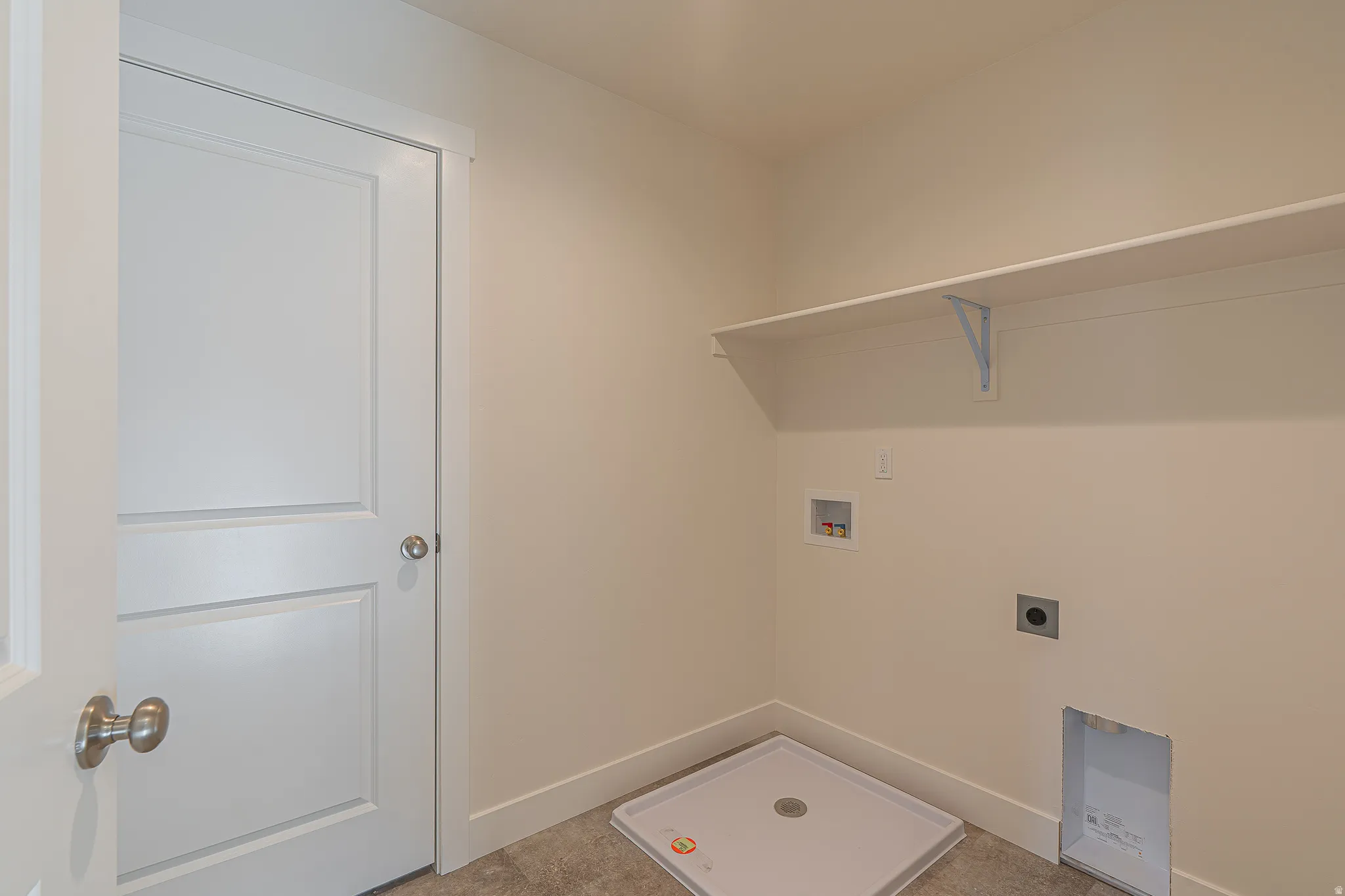 Dedicated utility area featuring a white wall shelf, appliance hookups, and a pre-installed washer pan