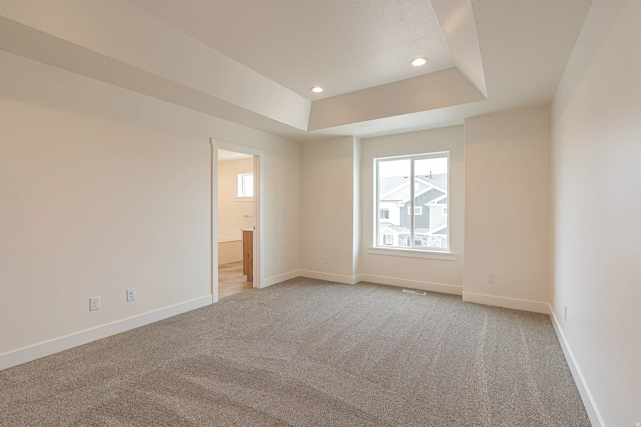 Spacious room with tray ceiling, recessed lighting, carpet flooring, and a large window