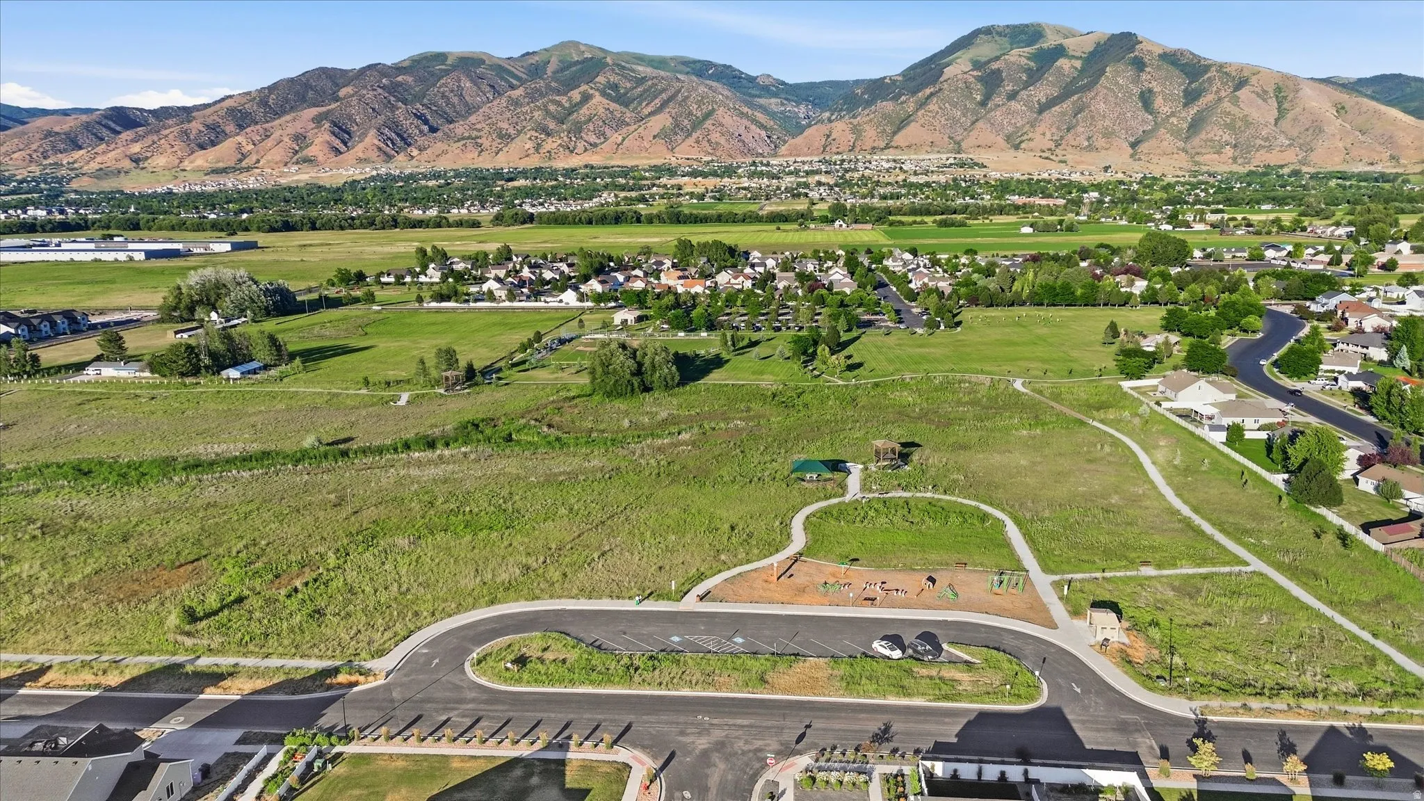 Expansive undeveloped land featuring a paved roadway, a dedicated parking area, and a recreational space with play equipment