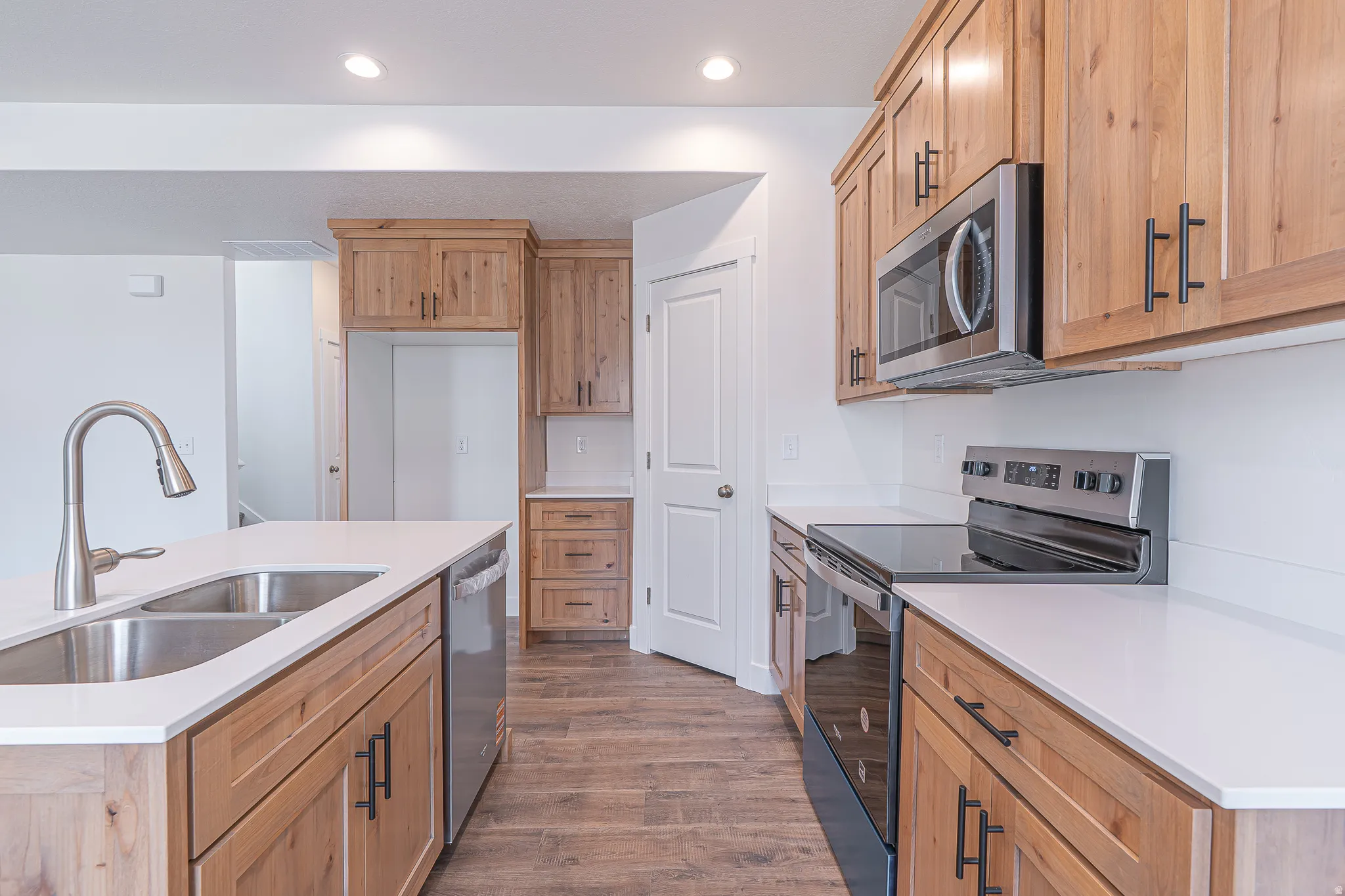 Kitchen featuring light wood cabinetry, white countertops, stainless steel appliances, and wood-finish flooring