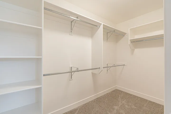 Walk-in closet featuring built-in shelving, multiple hanging rods, white walls, white baseboards, and a neutral-toned carpeted floor
