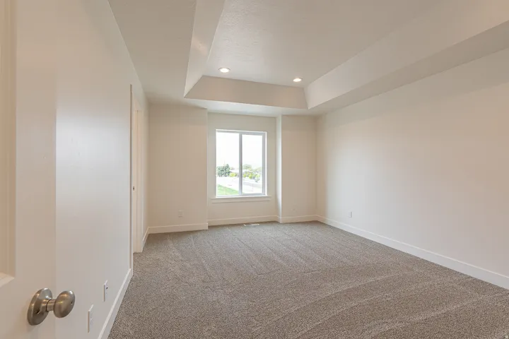 Spacious room featuring neutral carpeting, a tray ceiling with recessed lighting, and a multi-pane window