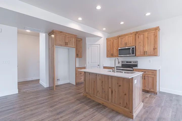 Kitchen featuring wood-finish cabinetry, stainless steel appliances, a center island with sink, white countertops, and recessed lighting