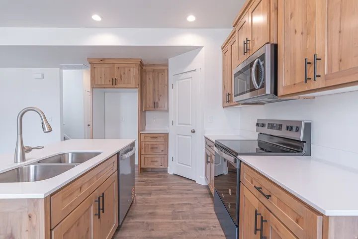 Kitchen featuring light wood cabinetry, white countertops, stainless steel appliances, and wood-finish flooring