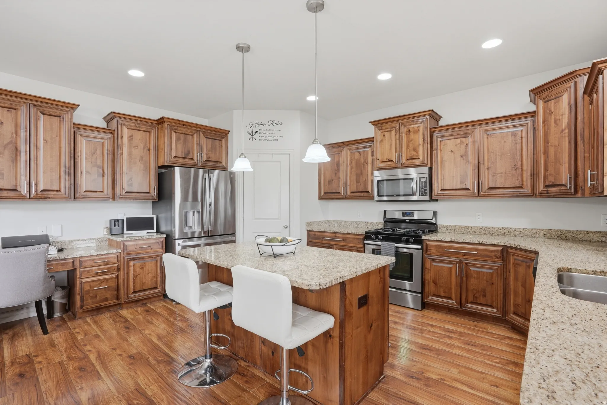 Spacious kitchen featuring an island with pendant lighting, wood-finish flooring, recessed lighting, stainless steel appliances, and ample cabinetry with granite countertops