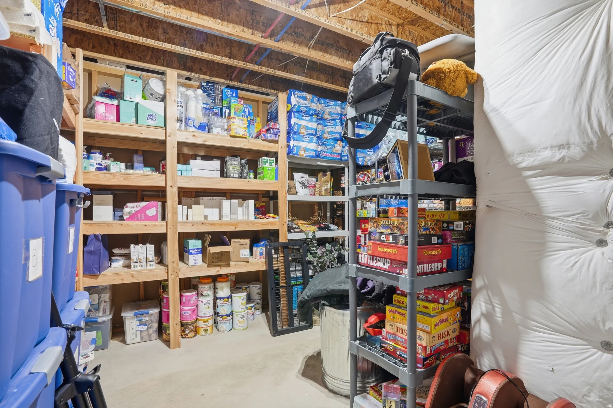 Spacious storage area featuring exposed ceiling joists, concrete flooring, and multiple shelving units