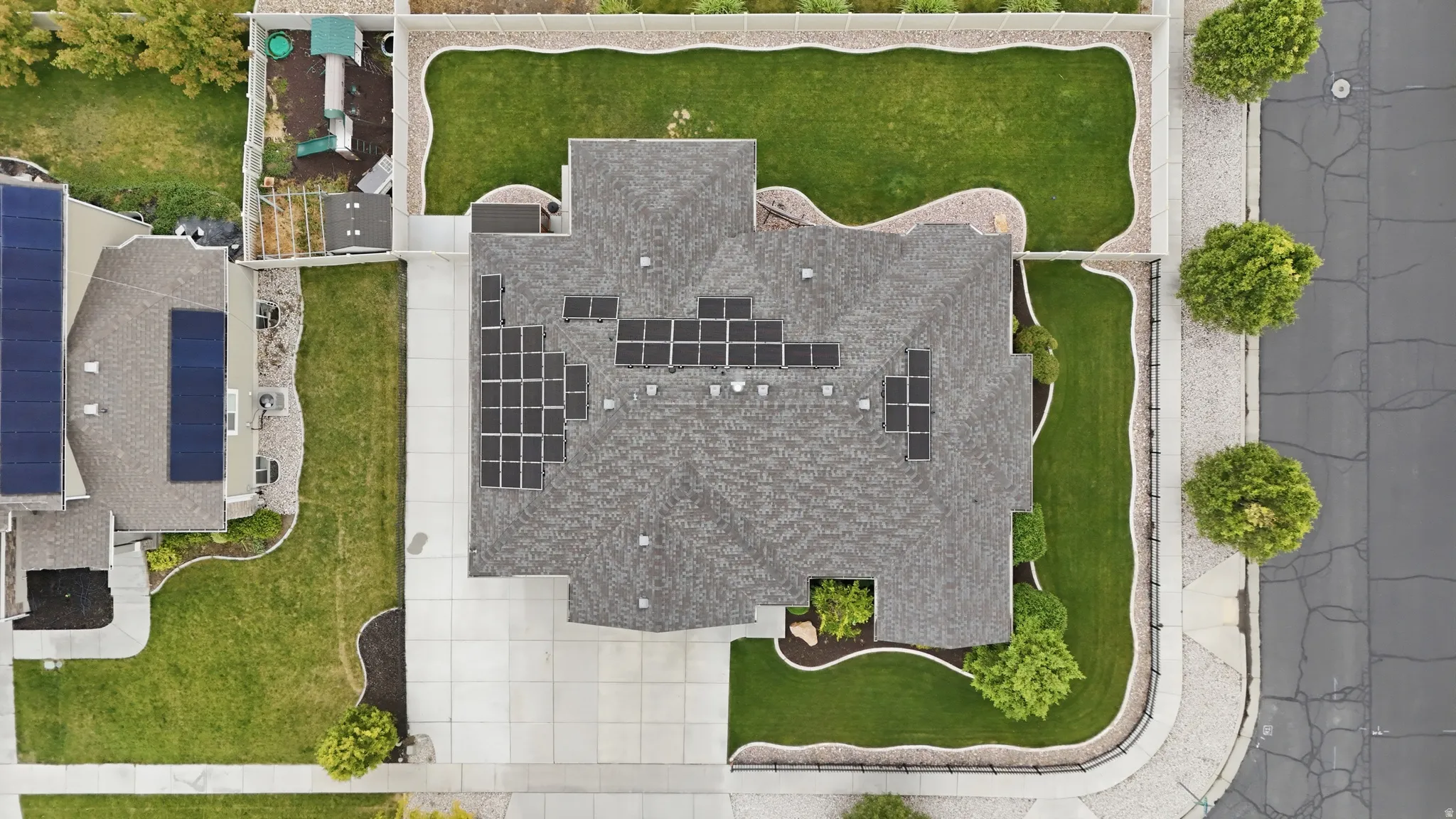 Aerial view of a residential property featuring a gray shingle roof, multiple solar panels, a concrete driveway, and a manicured lawn
